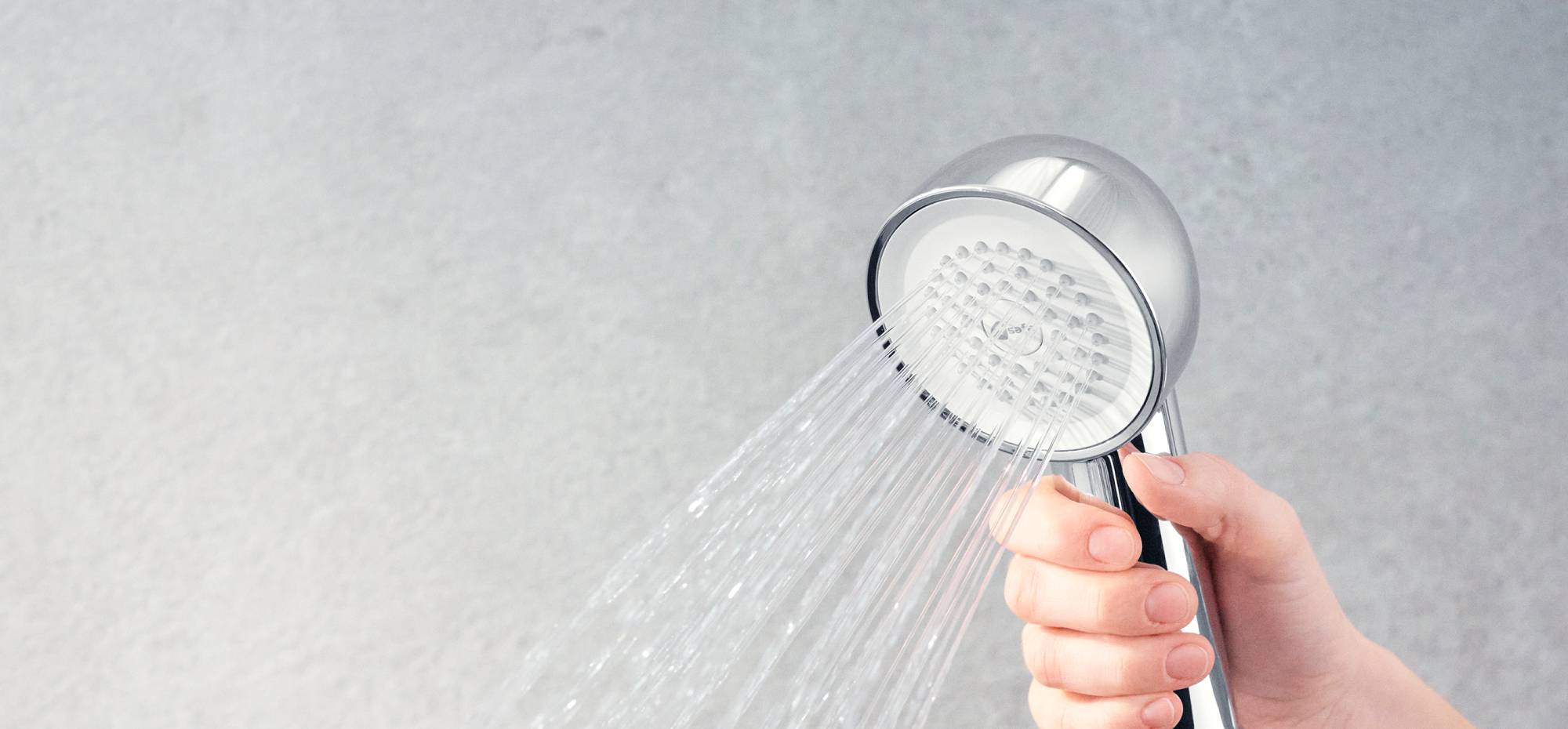 Hand holding Chrome Hand Shower Filter on a grey background.