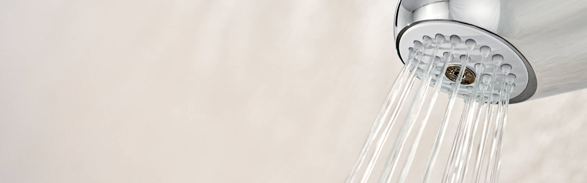 Close up of the Chrome Wall Shower Filter on a light wall, with water flowing from the nozzle.