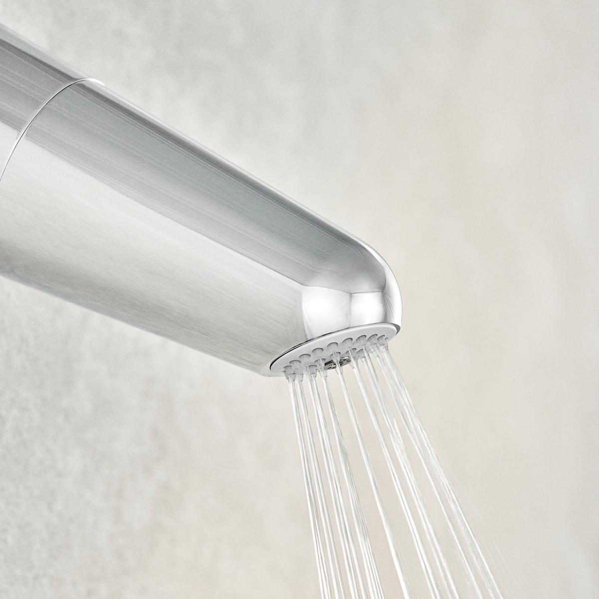Close up of the Chrome Wall Shower Filter on a grey wall, with water flowing from the nozzle.