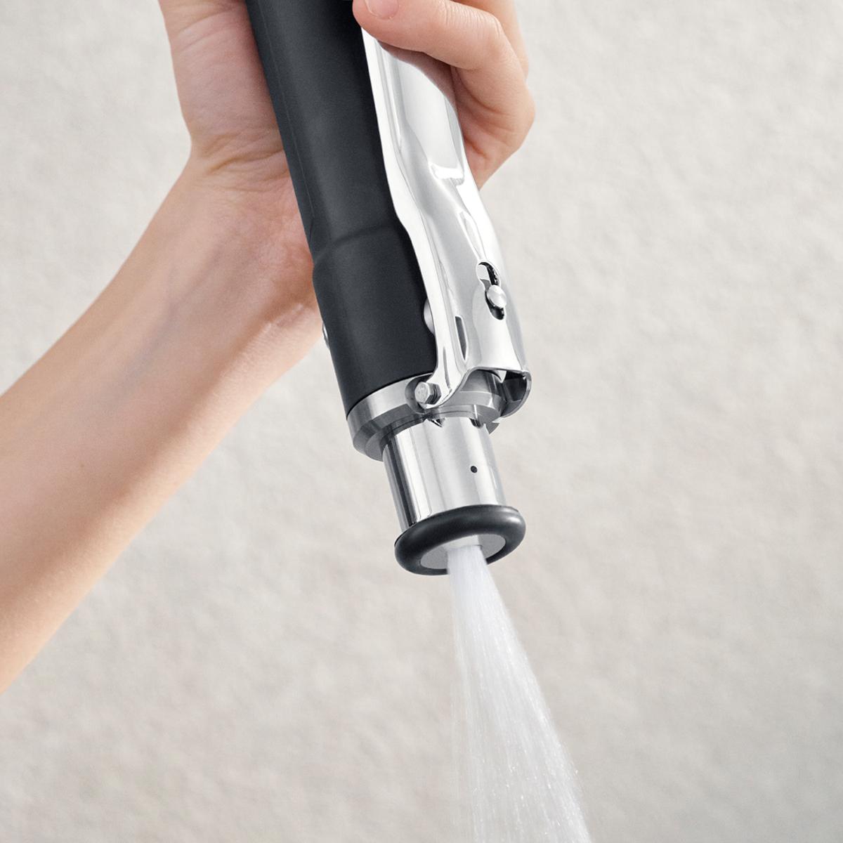 A person holding the Kitchen Spray Filter showcasing its sleek design, with water spraying out.