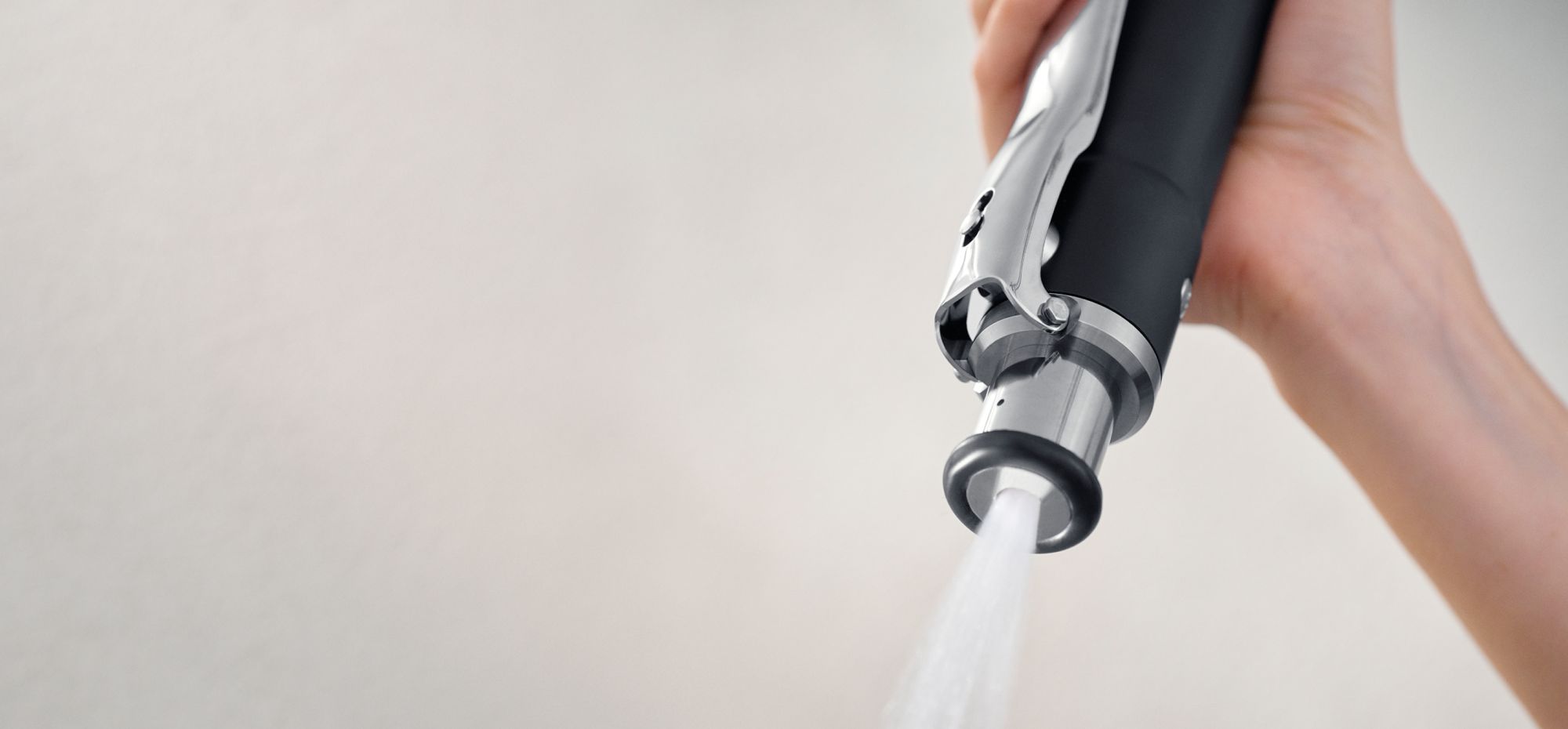 A person holding the Kitchen Spray Filter showcasing its sleek design, with water spraying out.